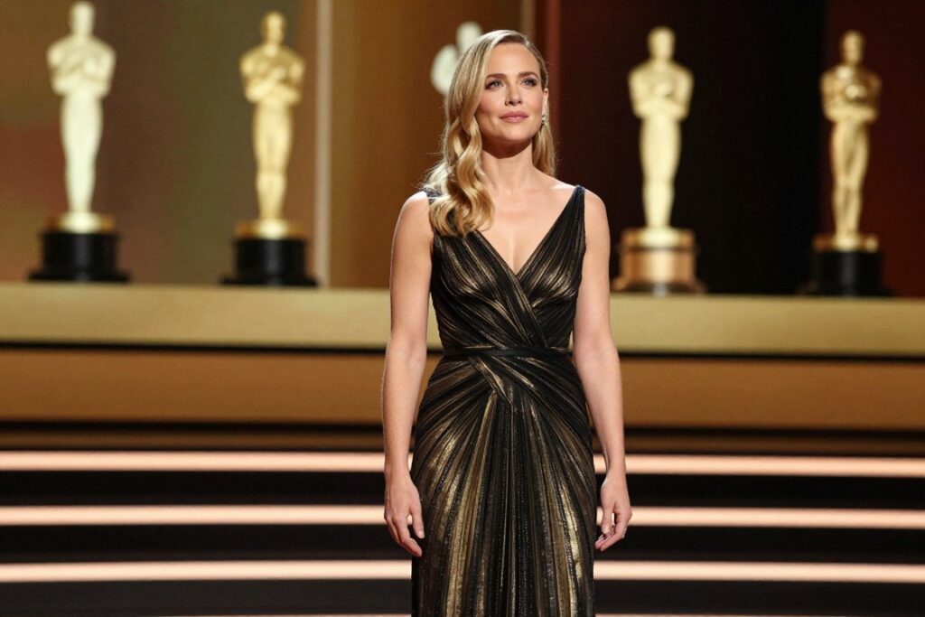 A confident and poised Kate Hudson stands in a dramatic spotlight, symbolizing her career evolution. She wears an elegant black and gold evening gown, exuding sophistication and determination. In the foreground, her expression is one of inspiration and focus, showcasing her journey in the film industry. The middle ground features a cinematic stage with soft golden lighting, creating an atmosphere of celebration and achievement. In the background, blurred silhouettes of iconic film awards and accolades subtly hint at her impactful contributions to cinema. The overall mood is uplifting and triumphant, capturing the essence of a pivotal moment in her career. The composition should be framed with a slight upward angle, emphasizing her stature as a leading actress on the rise.